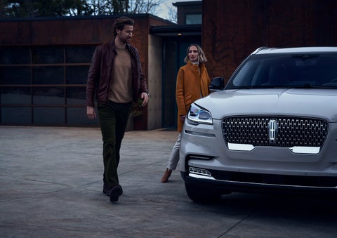 A man and a woman approaching a 2024 Lincoln Aviator® SUV, which illuminates certain lights when they are close | Thomasville Lincoln in Thomasville GA