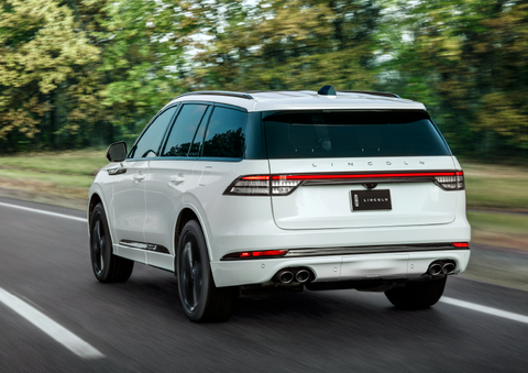 A white 2025 Lincoln Aviator® SUV is being driven away down a road lined with colorful trees. | Thomasville Lincoln in Thomasville GA