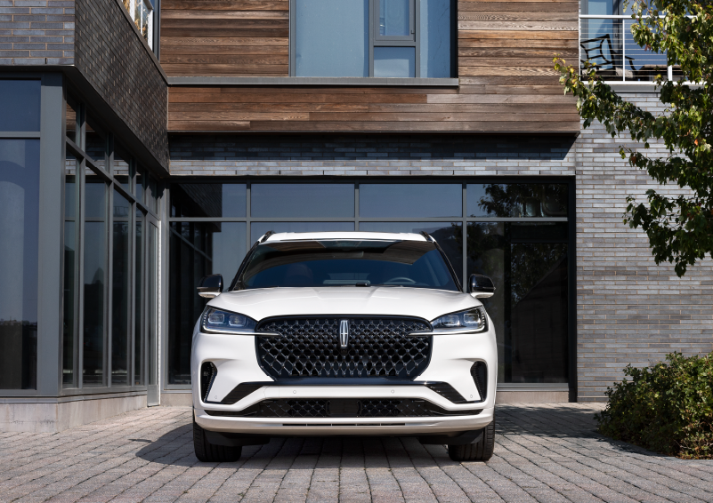 A white 2025 Lincoln Aviator® SUV is shown parked outside a modern building with gray brick and wood accents. | Thomasville Lincoln in Thomasville GA