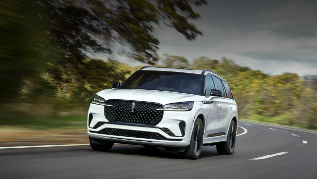 A white 2025 Lincoln Aviator® SUV is being driven down a road lined with trees. | Thomasville Lincoln in Thomasville GA