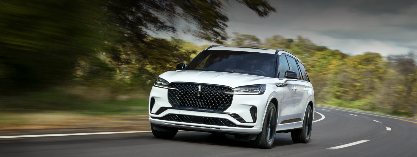 A white 2025 Lincoln Aviator® SUV is being driven down a road lined with trees. | Thomasville Lincoln in Thomasville GA